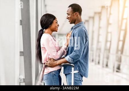 Amando l'uomo afroamericano e la donna coccolarsi nel terminal dell'aeroporto Prima del volo Foto Stock