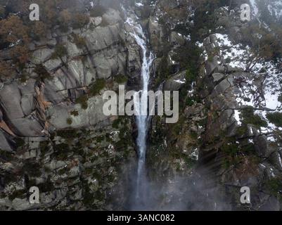 Vista aerea di una cascata mozzafiato che si getta sulle scogliere rocciose circondate da alberi innevati e nebbia, Mount Buffalo, Victoria, Australia. Foto Stock