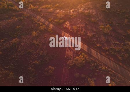 Vista aerea del tranquillo tramonto sul paesaggio aspro con strada e veicolo aperti, il Parco Nazionale di Karijini, Australia Occidentale. Foto Stock