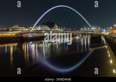 Newcastle, Regno Unito - 13 aprile 2025 - Vista notturna dell'iconico ponte del millennio di gateshead che attraversa il fiume Tyne con Sage Gateshead e Tyne Bridge in th Foto Stock