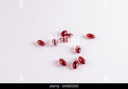 Capsule di gelatina ovale rossa con vitamina e, un integratore attivo sono sparse su sfondo bianco. Il concetto di miglioramento della salute , ringiovanimento Foto Stock