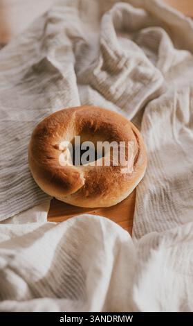 Una ciambella rotonda, marrone e leggermente bruciata si trova su un panno bianco. La ciambella è posta su una superficie di legno e il panno è sparso per creare un'atmosfera accogliente Foto Stock