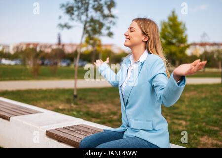 Donna d'affari felice con le braccia allungate, godendosi un momento di relax nel parco, sentendosi libera e gioiosa. Foto Stock