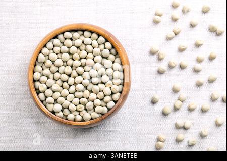 Piselli verdi essiccati in un recipiente di legno su lino. Semi di Pisum sativum, una coltura a impulsi, vegetale o foraggio, che possono essere ricostituiti in acqua calda. Foto Stock
