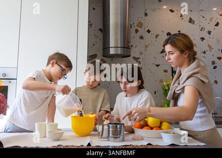 Madre e figli cucinano insieme in cucina. Una madre e i suoi tre figli cuocono insieme in una cucina moderna, mescolando gli ingredienti in ciotole e. Foto Stock