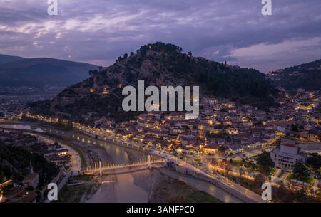 Vista aerea della città storica di Berat con architettura medievale illuminata dalle luci serali lungo il fiume Osum, Berat, Albania. Foto Stock