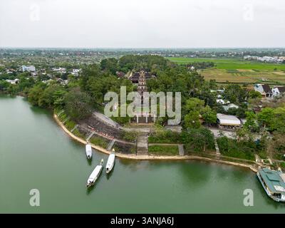 Vista aerea della tranquilla Pagoda di Thien Mu vicino al tranquillo fiume circondato da vegetazione lussureggiante e barche, Thuy Bieu, Hue, Thua Thien Hue, Vietnam. Foto Stock