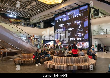 Regno Unito, Inghilterra, aeroporto di Manchester, sala partenze Terminal 2, passeggeri in attesa su un gigantesco schermo pubblicitario Foto Stock