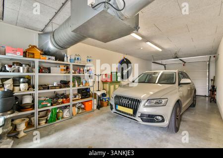 Un garage ben illuminato che mostra un SUV argentato parcheggiato accanto agli scaffali con vari attrezzi e attrezzature organizzati, sottolineando funzionalità e spazio. Foto Stock