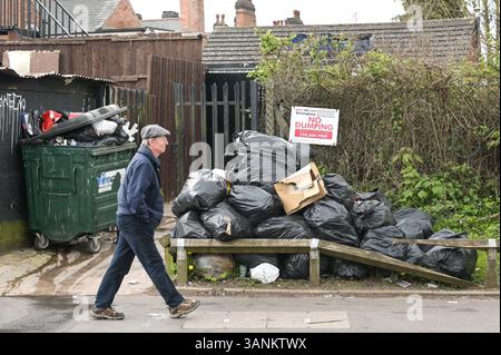 Spring Road, Acocks Green, Birmingham, 15 aprile 2025: Un uomo cammina davanti ai rifiuti sorvolati dalla mosca in Spring Road a Birmingham. – Poiché i lavoratori dei rifiuti continuano a scioperare con il sostegno dell’Unione Unite, le aree di Birmingham soffrono ancora perché i rifiuti vengono lasciati fuori dalle case e dalle imprese. Una grande pila di sacchetti è stata lasciata di fronte a un cartello "No dumping" che avverte di multe fino a 20.000 kg su Spring Road, nella zona di Acocks Green della città. Crediti: British News and Media/Alamy Live News Foto Stock