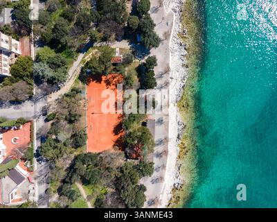 Vista aerea della pittoresca costa con una spiaggia tranquilla e un vivace campo da tennis circondato da una vegetazione lussureggiante, Novi Vinodolski, Croazia. Foto Stock
