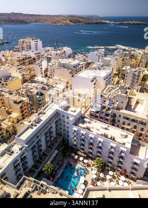 Vista aerea di una vivace festa in piscina in un lussuoso resort vicino allo splendido oceano, St. Paul's Bay, Malta. Foto Stock