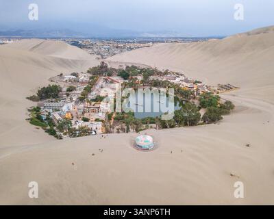 Vista aerea dell'oasi desertica di Huacachina e delle luci della città sullo sfondo, Perù. Foto Stock
