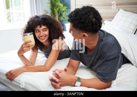 Coppia che condivide il caffè mattutino, rilassandosi e sorridendo in una camera accogliente Foto Stock