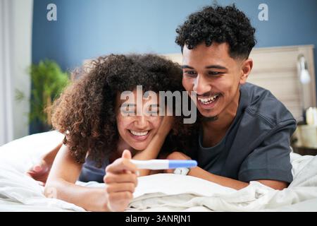 Felice coppia sorridente eccitato a casa con un test di gravidanza positivo Foto Stock