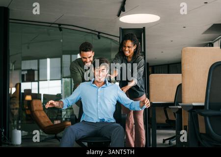 I giovani colleghi si divertono insieme a cavalcare sulle sedie in ufficio e lavorare in ufficio con persone molto eccitate Foto Stock