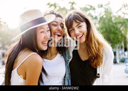 Tre giovani donne sorridenti che ridono insieme camminando in strada cittadina Foto Stock
