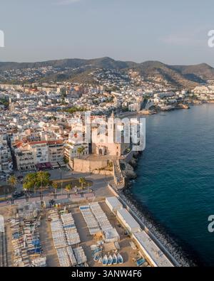 Vista aerea della splendida città costiera con chiesa storica e montagne panoramiche che si affacciano sul mar mediterraneo, Sitges, Spagna. Foto Stock