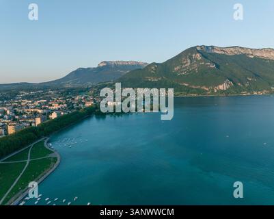 Vista aerea del tranquillo lago di Annecy, circondato da montagne pittoresche e da un vivace paesaggio urbano al tramonto, Annecy, Francia. Foto Stock