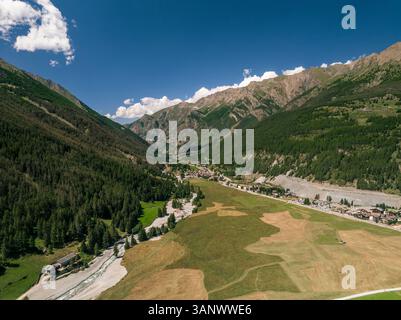 Vista aerea di un pittoresco villaggio circondato da maestose montagne e vegetazione lussureggiante in Valle d'Aosta, Italia. Foto Stock