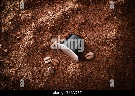 Sfondo caffè espresso con una capsula di alluminio nero su una pila di caffè macinato e diversi chicchi di caffè tostati accanto ad essa. Vista dall'alto. Foto Stock