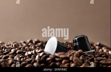 Dettaglio delle capsule di caffè espresso in alluminio nero su una pila di chicchi di caffè tostati con sfondo marrone isolato. Vista frontale. Foto Stock