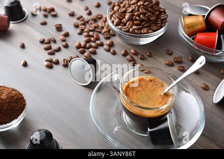Caffè espresso in una tazza di vetro su una panca di legno in una cucina con contenitori con capsule per caffè in polvere e chicchi. Vista dall'alto in alto. Foto Stock