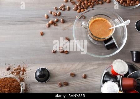 Caffè espresso in una tazza di vetro su una panca di legno in una cucina con contenitori con capsule per caffè in polvere e chicchi. Vista dall'alto. Foto Stock