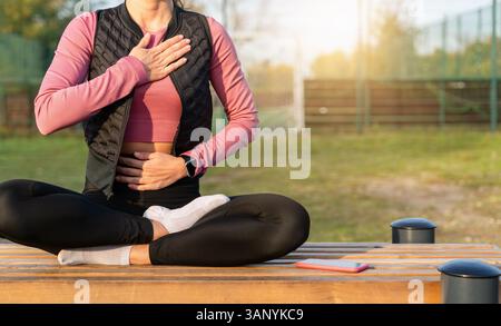 Donna in forma che fa esercizio respiratorio in posizione di loto dopo l'allenamento all'aperto Foto Stock