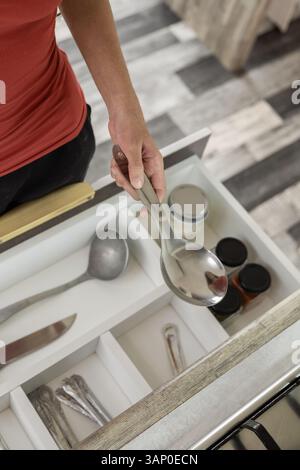 Una prospettiva alternativa di un cassetto aperto che rivela utensili da cucina organizzati, come cucchiai, mestoli, coltelli, forchette e altro ancora, all'interno di un'elegante e moderna cabina in legno Foto Stock
