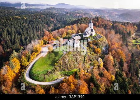 Vista aerea di un pittoresco paesaggio autunnale con una chiesa storica e una cappella su una collina circondata da una tranquilla foresta, Sternberg, Carinzia, Au Foto Stock