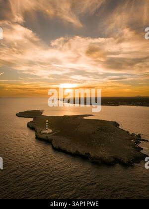 Vista aerea dello splendido tramonto sull'oceano tranquillo con faro a Cap de l'Isla de l'Aire, Punta prima, Sant Lluis, Isole Baleari, Spagna. Foto Stock