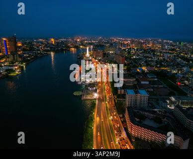 Veduta aerea del vivace paesaggio urbano con grattacieli illuminati e traffico intenso lungo il fiume, Lagos, Nigeria. Foto Stock
