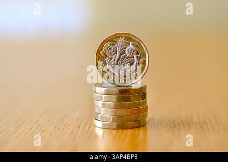 Una sola moneta britannica da una sterlina sul bordo di una scrivania con altre monete distese su uno sfondo defocalizzato Foto Stock