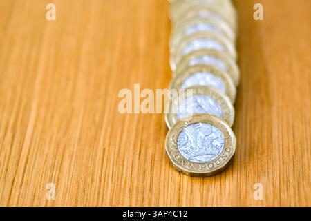 Una sola moneta britannica da una sterlina appoggiata su una colonna di monete da una sterlina su una scrivania Foto Stock