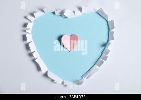 Carta bianca con foro a forma di cuore e rosa su sfondo azzurro, vista dall'alto Foto Stock