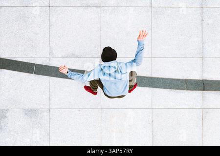 Vista aerea di uno skateboarder professionista che fa un kick flip sullo sfondo urbano nella piazza centrale della città di Kaunas, Lituania. Foto Stock