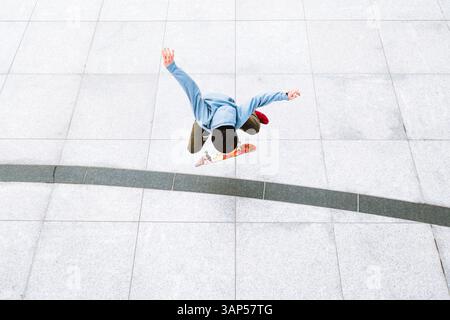 Vista aerea di uno skateboarder professionista che fa un kick flip sullo sfondo urbano nella piazza centrale della città di Kaunas, Lituania. Foto Stock