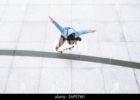 Vista aerea di uno skateboarder professionista che fa un kick flip sullo sfondo urbano nella piazza centrale della città di Kaunas, Lituania. Foto Stock