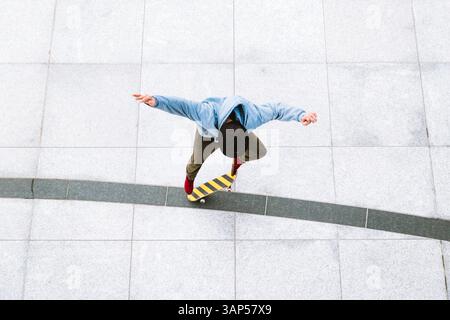 Vista aerea di uno skateboarder professionista che fa un kick flip sullo sfondo urbano nella piazza centrale della città di Kaunas, Lituania. Foto Stock