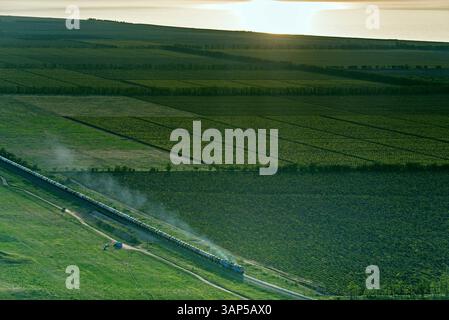 Vista aerea dei tranquilli campi agricoli con un treno che passa al tramonto, regione di Krasnodar, Russia. Foto Stock