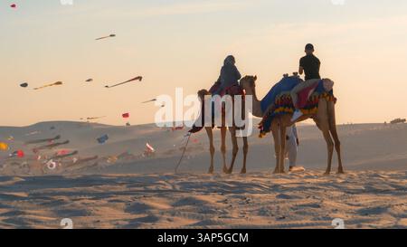 Doha, Qatar, 24 febbraio 2025: Un gruppo di persone che cavalcano cammelli attraverso le dune dorate del deserto, simboleggiando il viaggio spirituale e il patrimonio culturale del Ramadan. Foto Stock