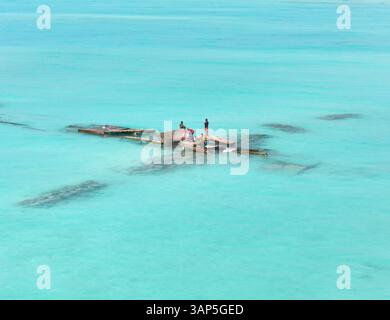 Vista aerea di una tranquilla isola tropicale con acque turchesi cristalline e persone su una zattera, Bileyfahi, Atollo Shaviyani, Maldive. Foto Stock