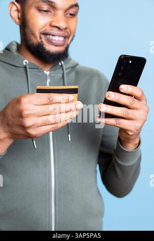 Felice uomo afroamericano che effettua un acquisto online con carta di credito, immettendo le credenziali bancarie per pagare qualcosa in promozione. Giovane ragazzo fiducioso che fa acquisti su Internet. Foto Stock