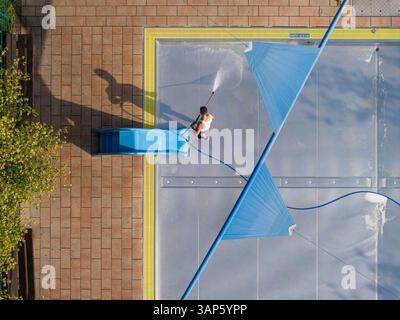 Vista aerea di una piscina pubblica con scivolo blu e addetto alle pulizie durante l'estate, matrimonio, Germania. Foto Stock