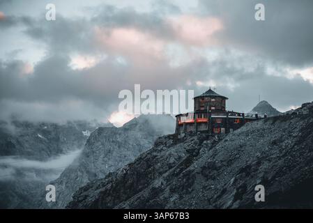 Stelvio, Italia - 29 giugno 2022: Veduta aerea delle maestose dolomiti con una cabina tranquilla tra cime rocciose e cielo nuvoloso, Stelvio, Italia. Foto Stock