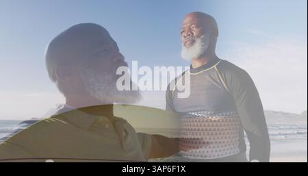 Composto da un anziano afroamericano che allunga le braccia e trasporta tavole da surf sulla spiaggia soleggiata Foto Stock