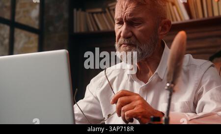 Vecchio uomo europeo caucasico imprenditore lavoratore d'affari mette su occhiali visione salute anziani iniziare lavoro laptop digitazione computer desktop finanza casa Foto Stock