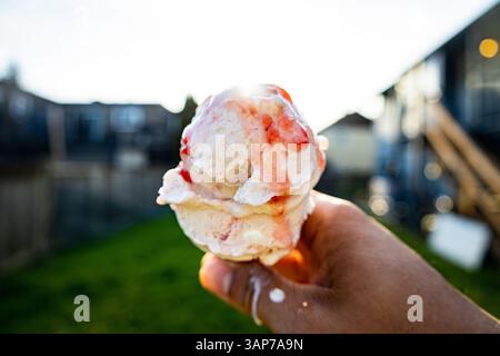 Tenere a mano il cono gelato alla fragola sul cortile posteriore con il sole dietro il cono Foto Stock