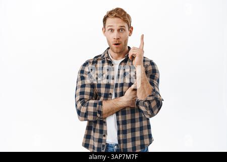 Ha avuto un'idea. Eccitato uomo adulto con capelli rossi, alzando il dito e dire suggerimento, pensare piano, trovato soluzione, mostrare eureka segno, in piedi su bianco Foto Stock